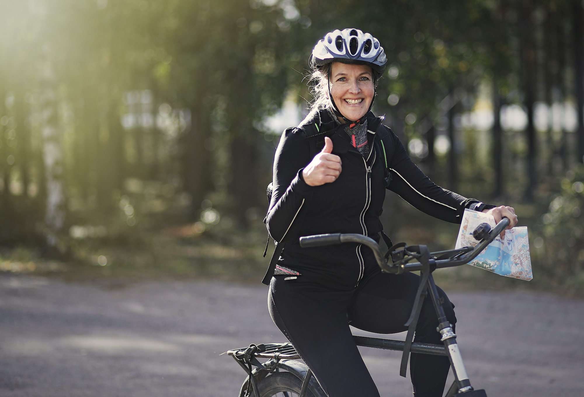 En kvinna på en cykel håller tummen uppåt medan hon håller en karta i andra handen.
