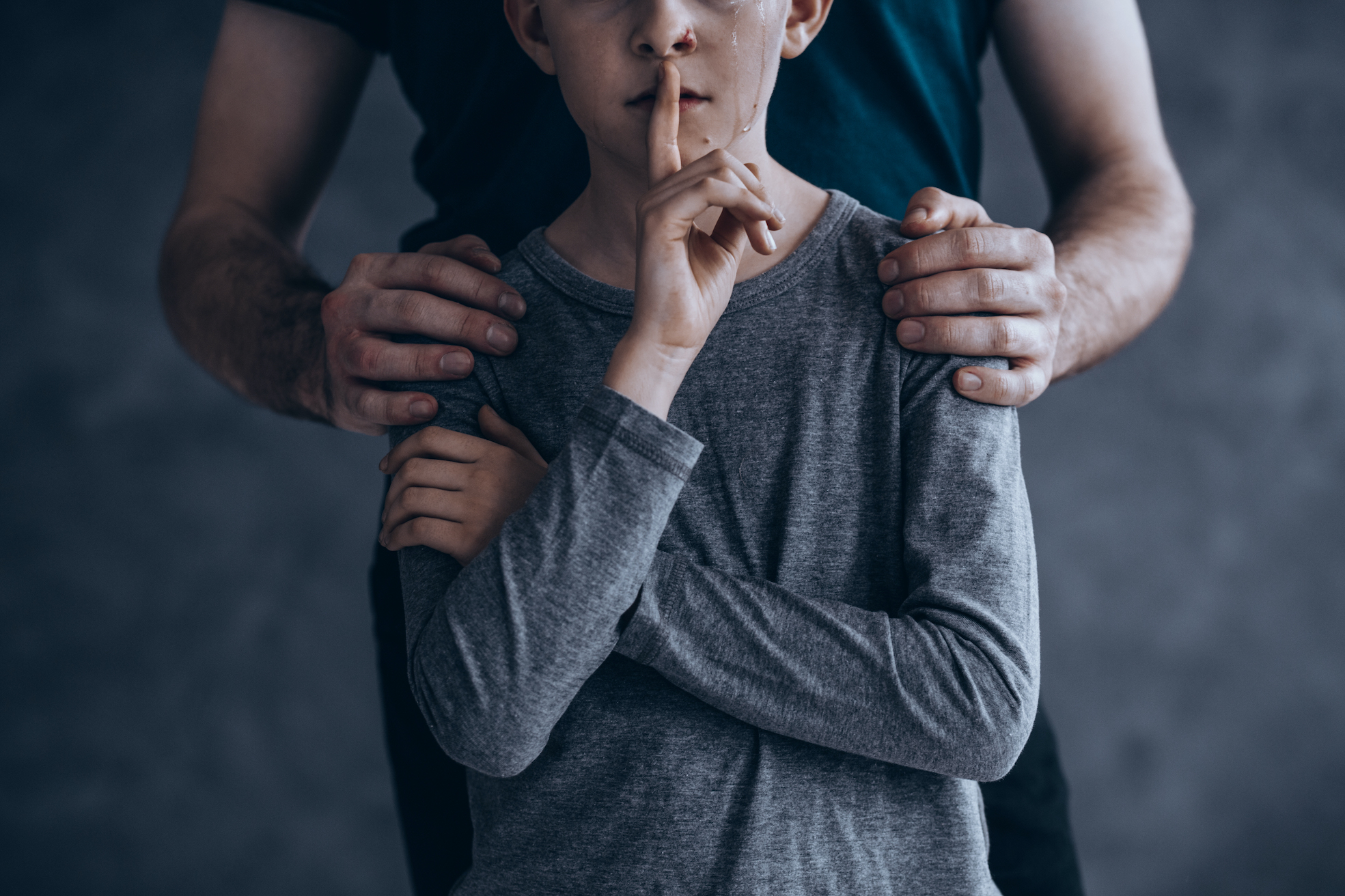 En pappa håller sina händer på sin sons axlar. Tårarna rinner ner för sonens ansikte. Sonen håller upp ett finger ovanför munnen.