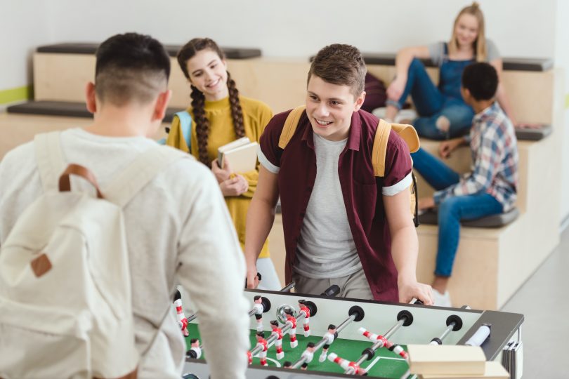 Två pojkar som spelar bordfotboll och en flicka tittar på