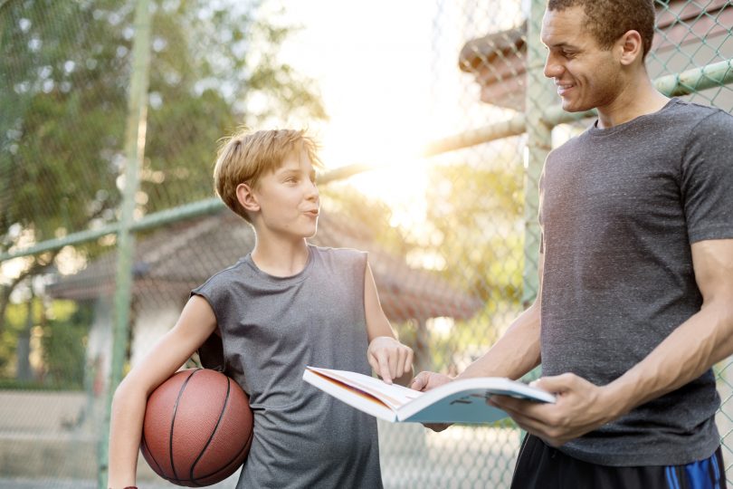 En ung pojke som står tillsammans med sin tränare och en basketboll under armen