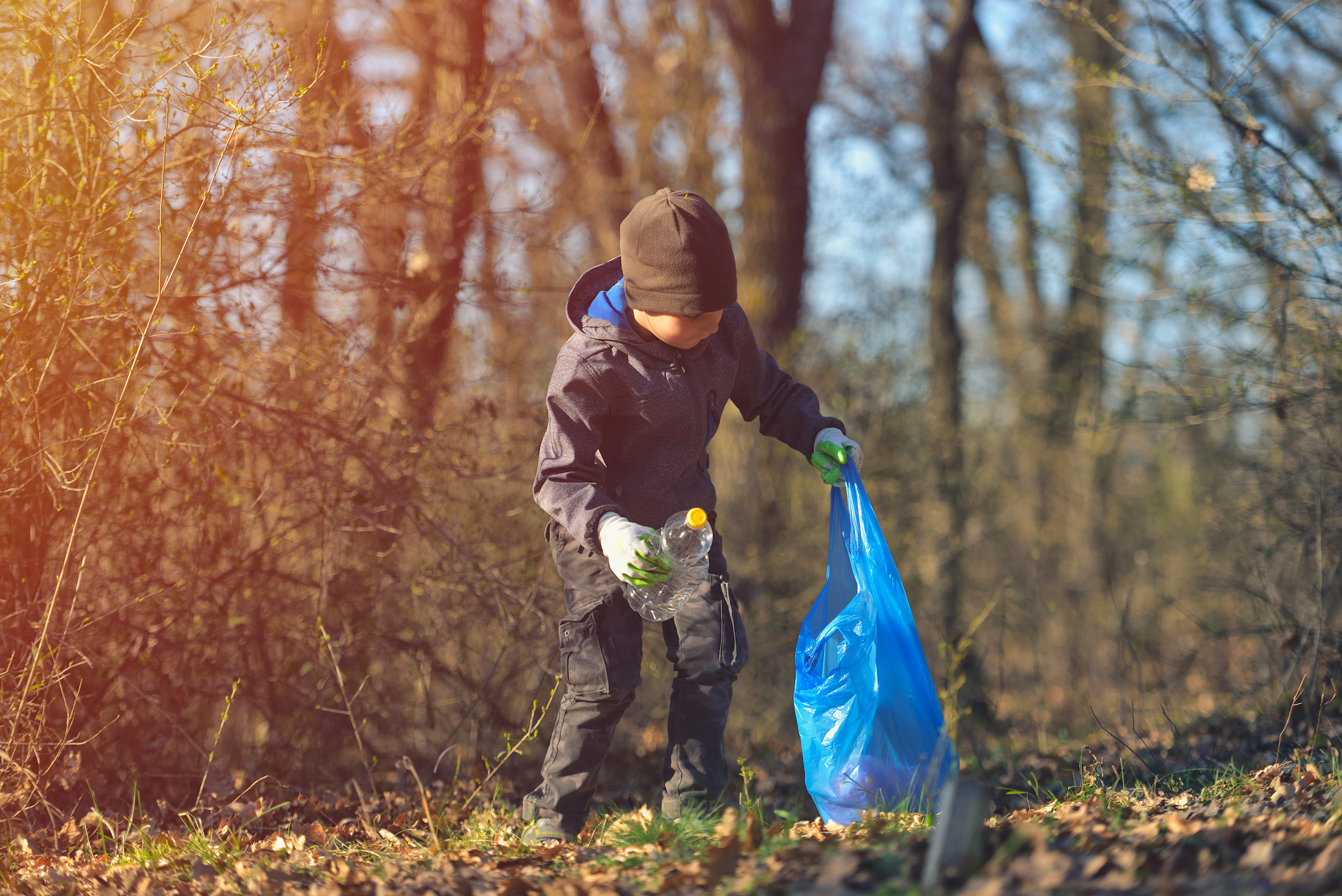 En pojke i skogen plockar upp en plast flaska och lägger den i en platspåse.