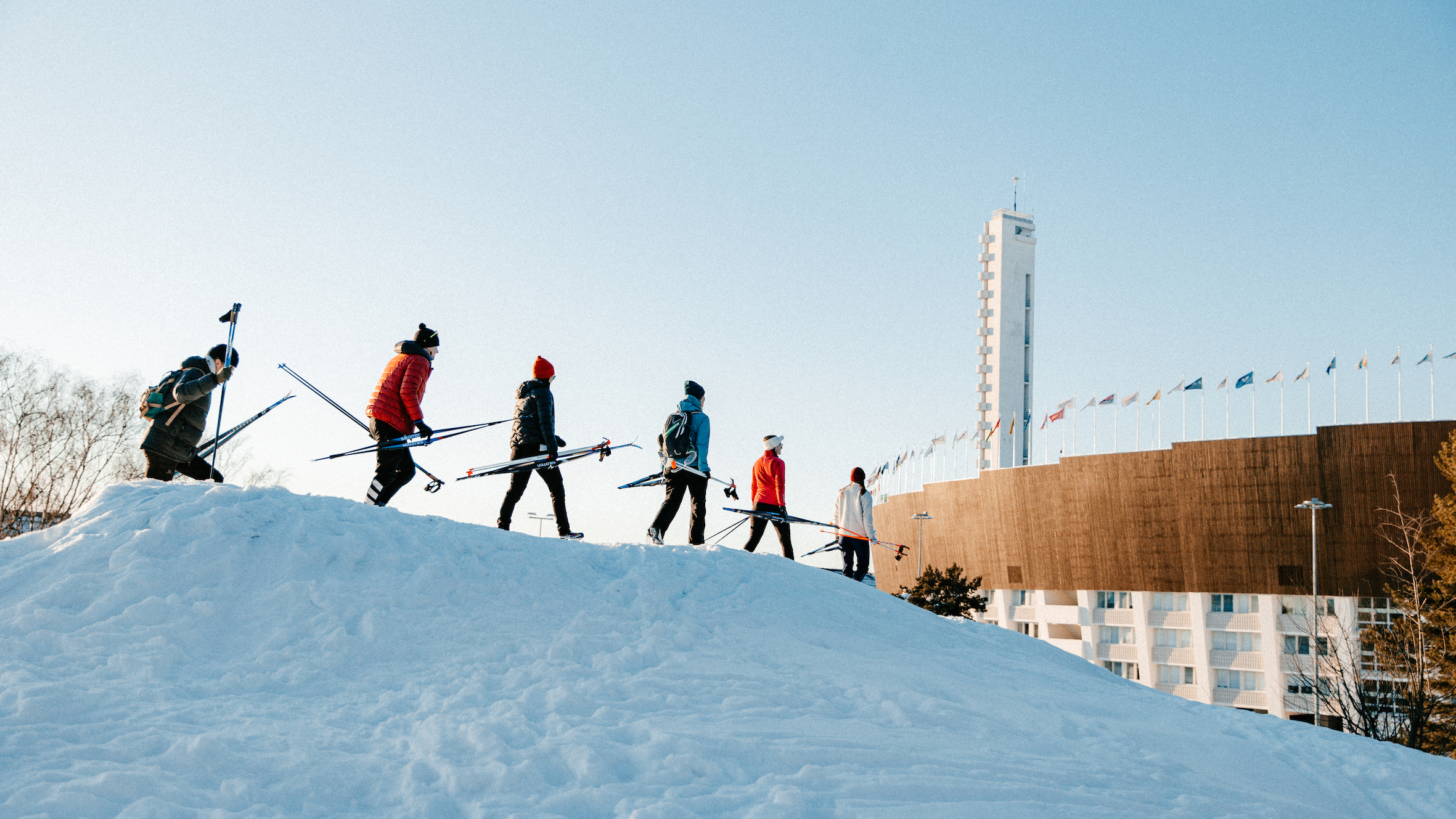 En grupp av människor med skidor och stavar går på nerför en snöbacke.
