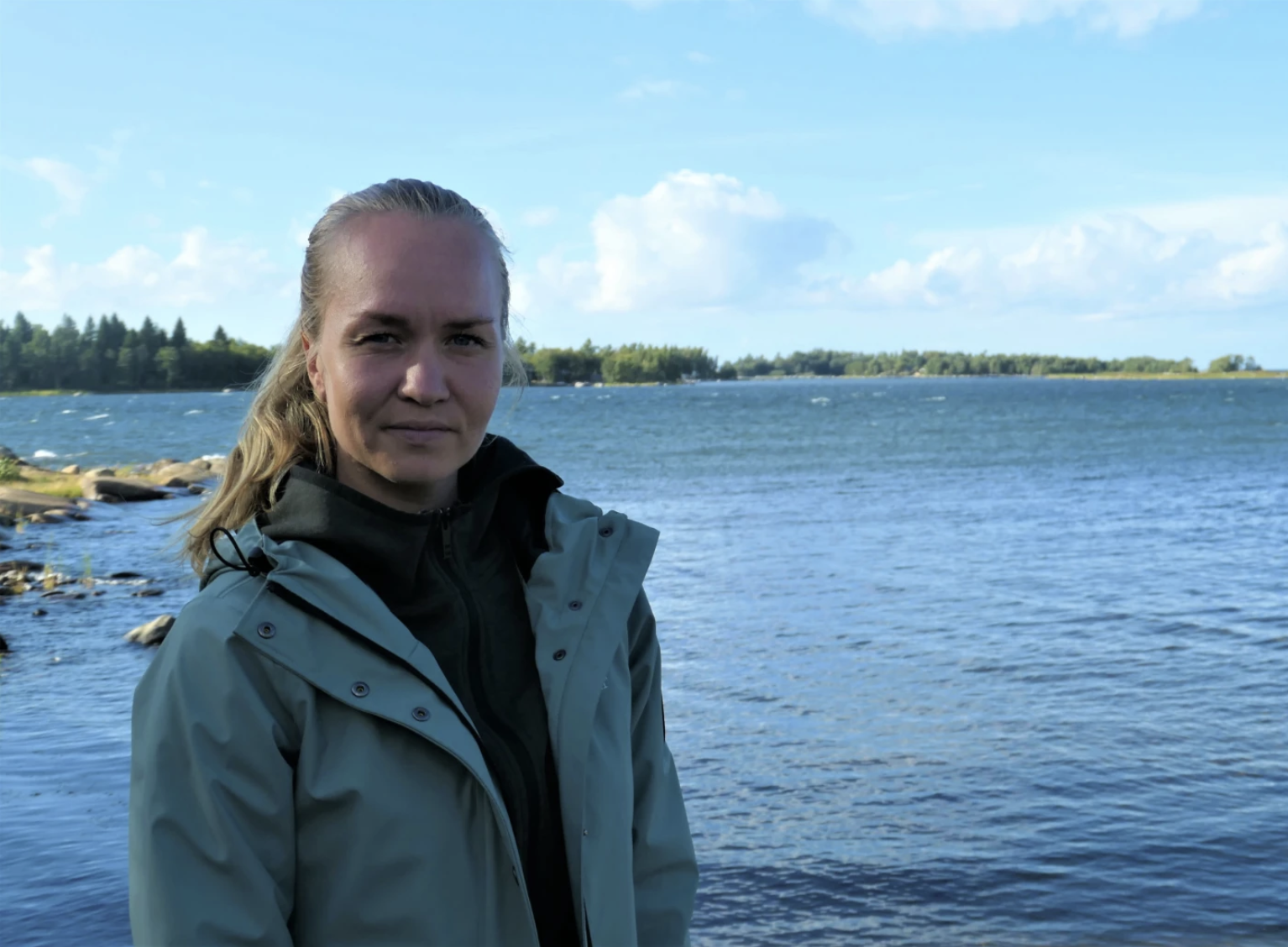 En privat bild på Jonna Skrifvars. Hon befinner sig utomhus nära en sjö.