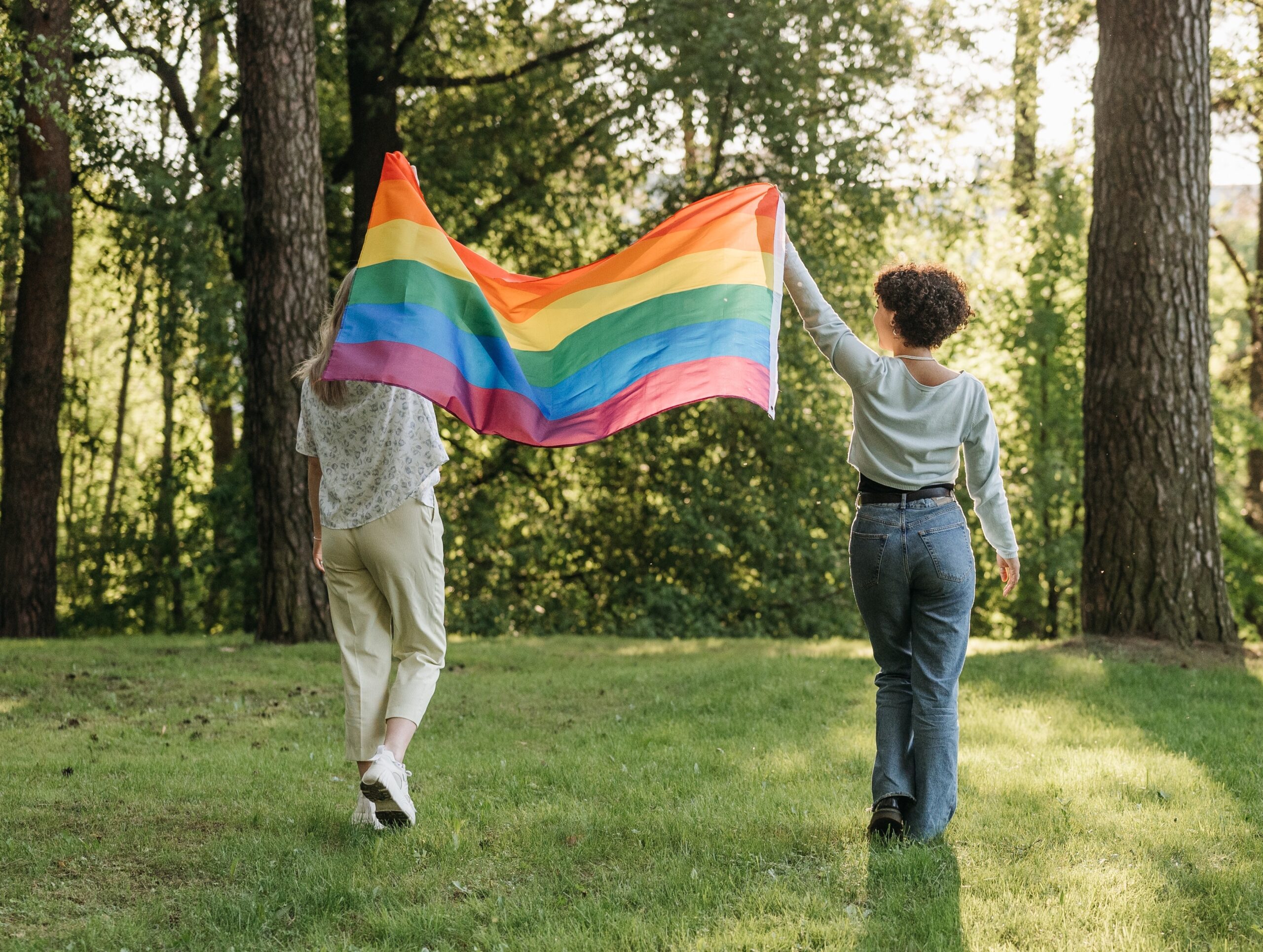 Två personer som håller upp en pride flagg i skogen.