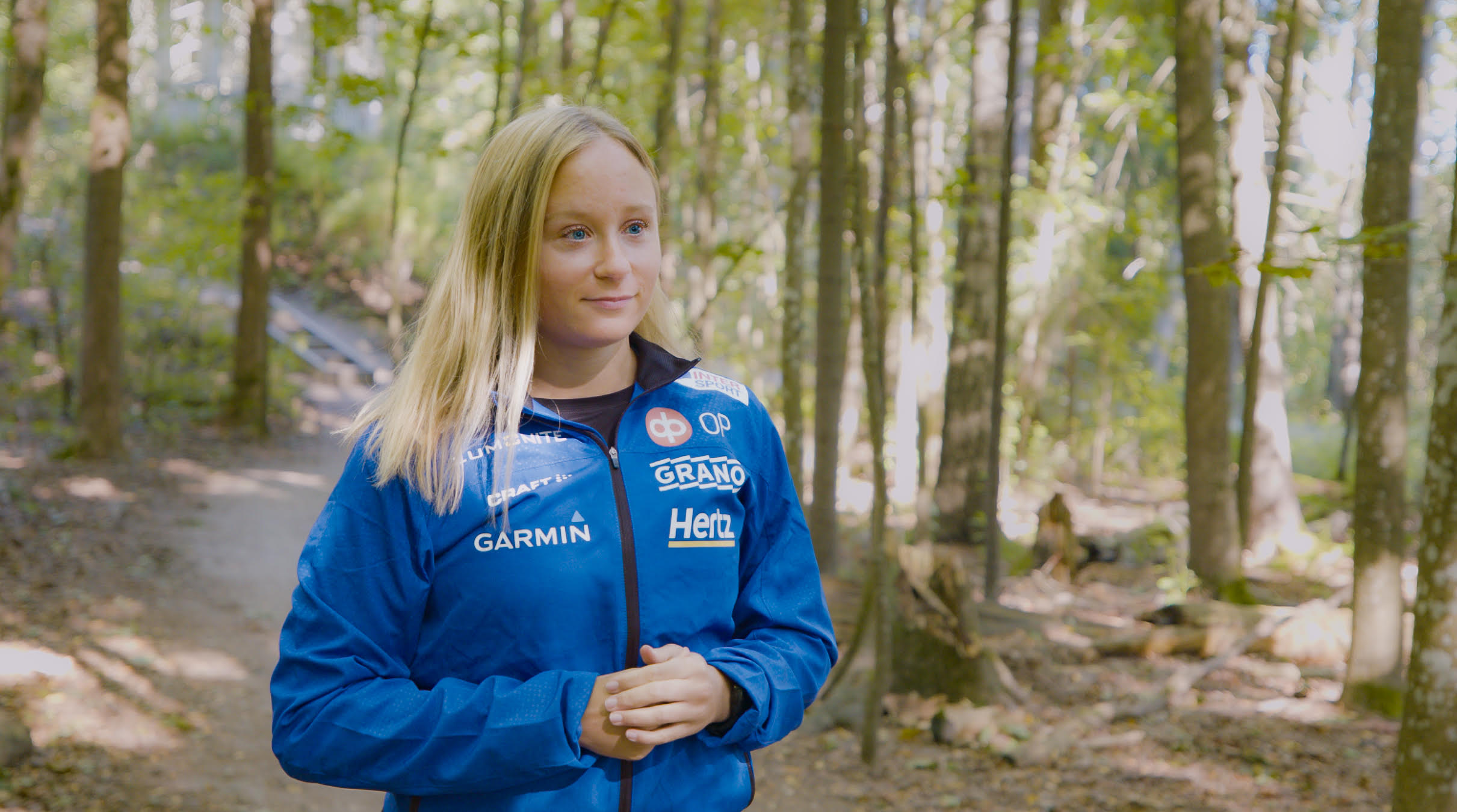 Lina Karlsson står ute i skogen. Han har blå träningskläder på sig.