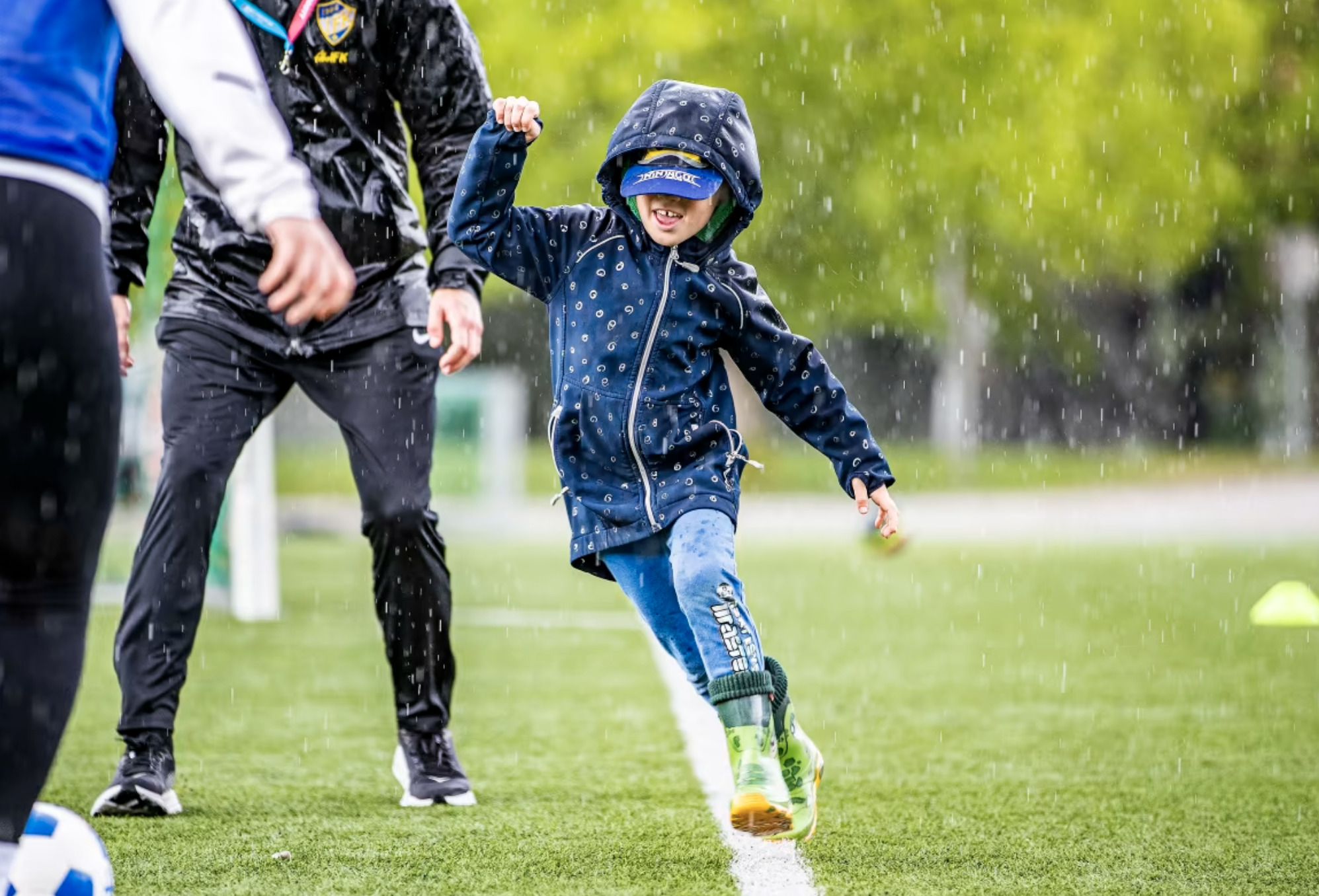 En ung pojke spelar fotboll i regnet